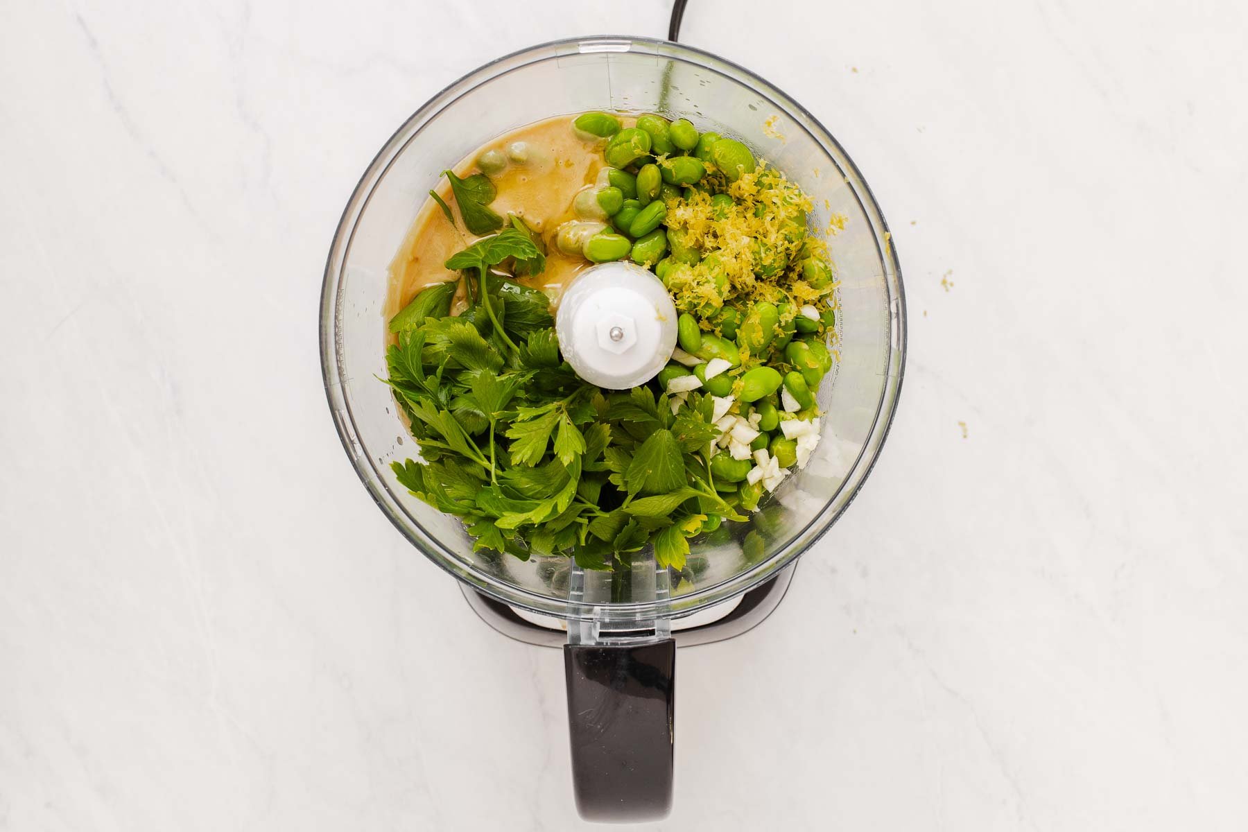 Food processor bowl with lemon zest, tahini, parsley and mukimame soy beans.