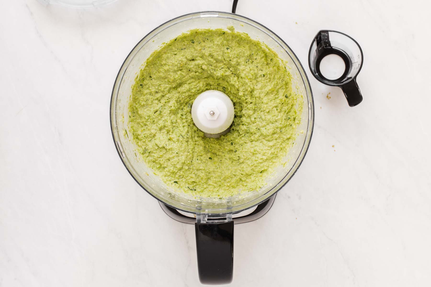 Bright green dip in mini food processor bowl on marble counter.