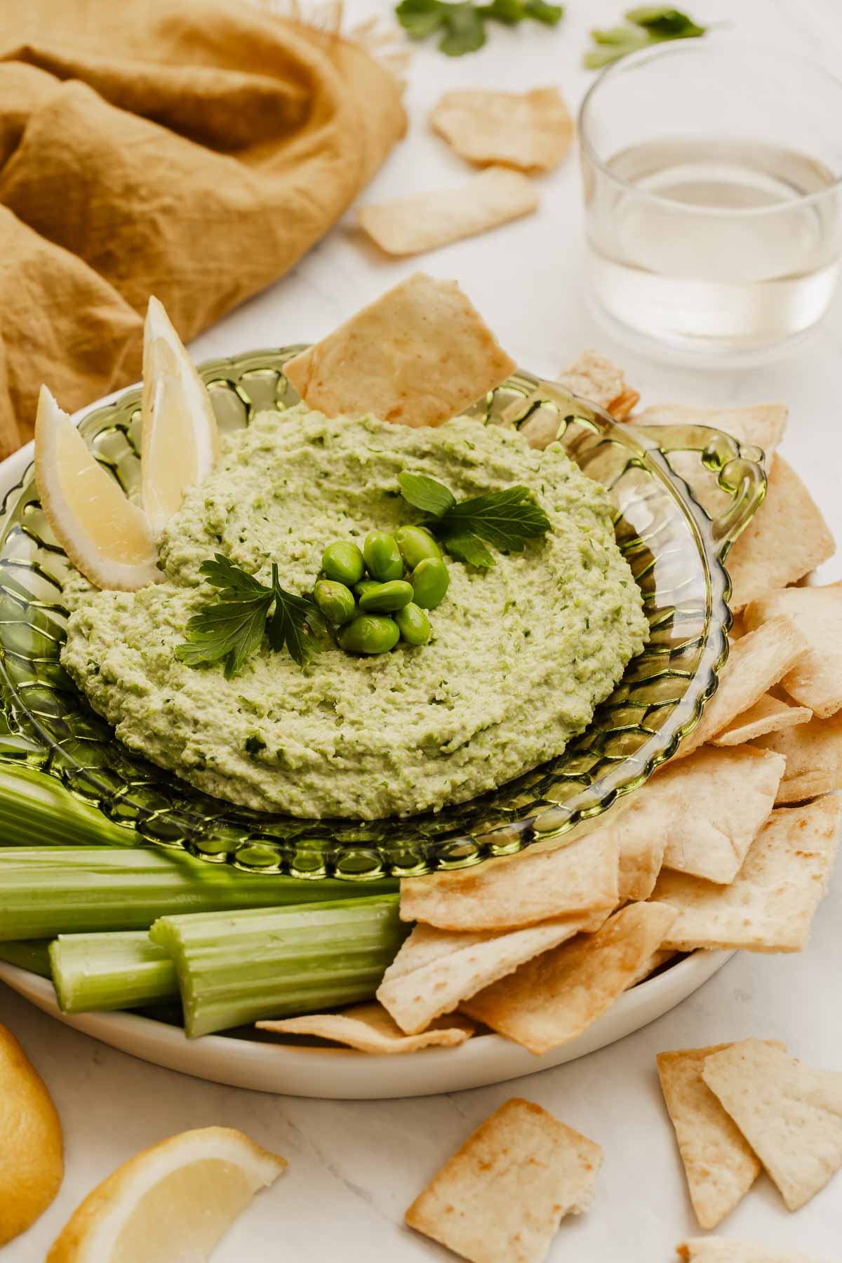 Edamame hummus on plate with pita chips and celery next to it.