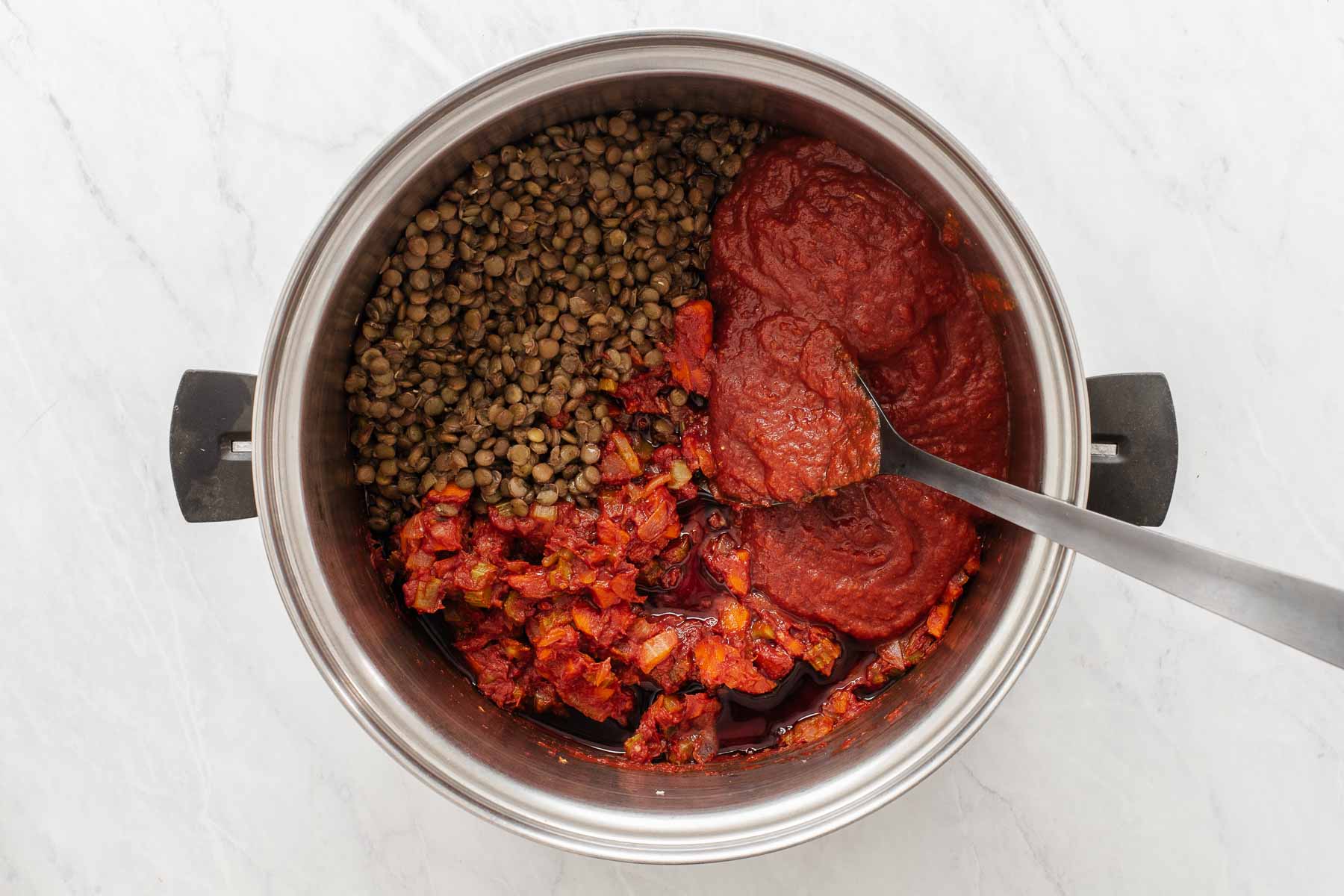 Adding tomato products to a pan with lentils in it.