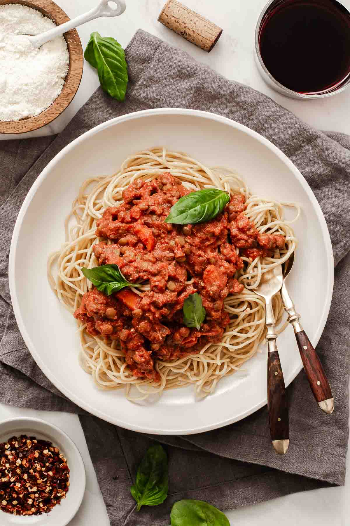 Vertical image of lentil bolognese over spaghetti on white plate with fresh basil.