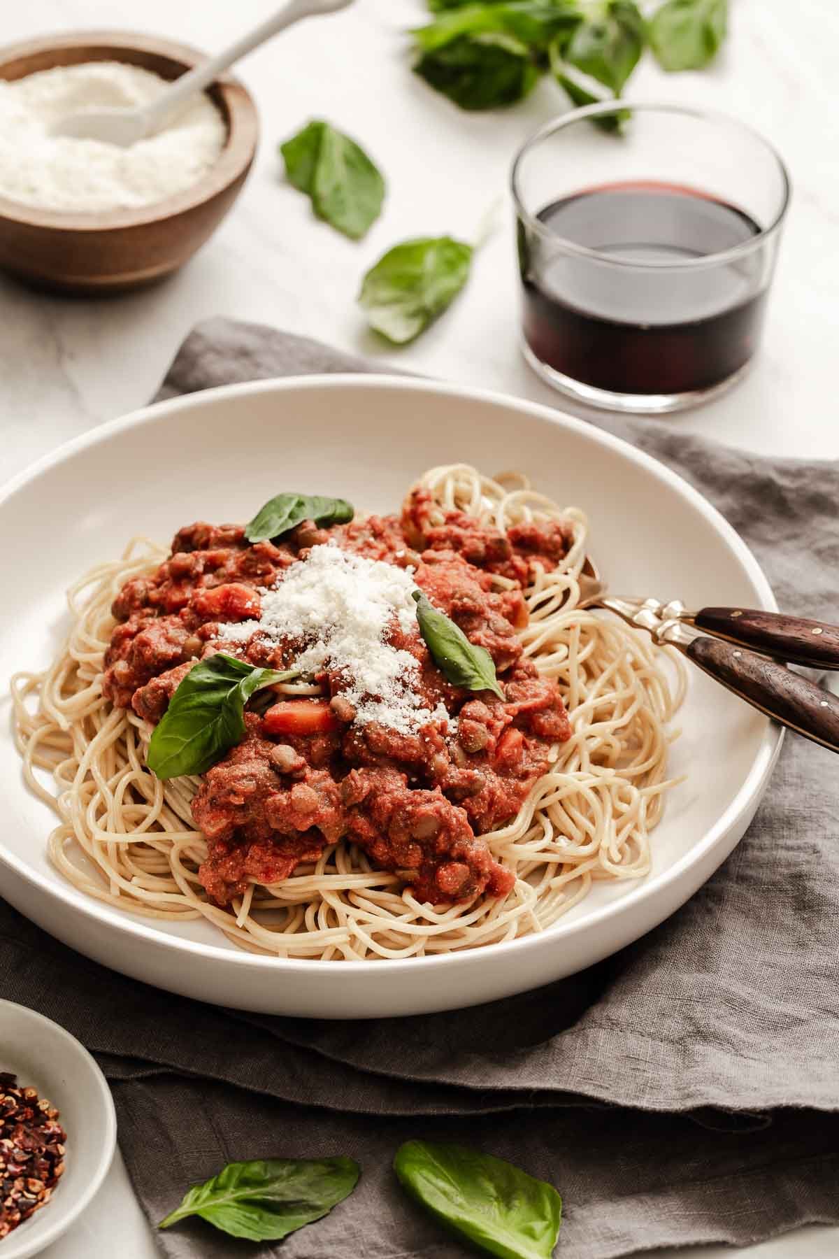 Vertical image of spaghetti and red lentil bolognese sauce on top.