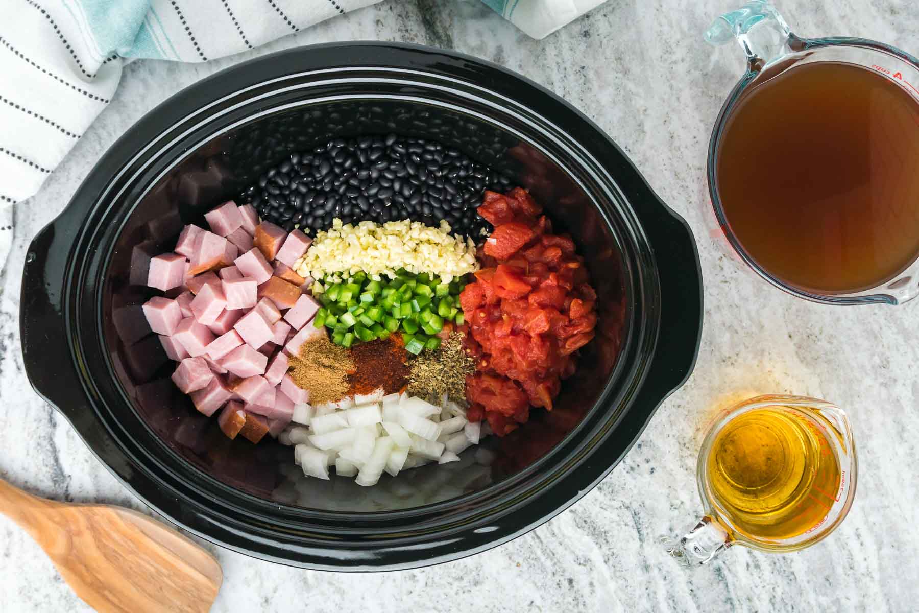 Diced ham, tomatoes, spices and vegetables in an oval black crock pot.
