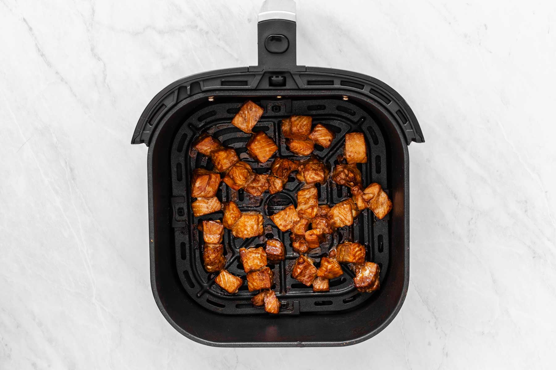 Teriyaki salmon cubes in an air fryer tray, cooked.