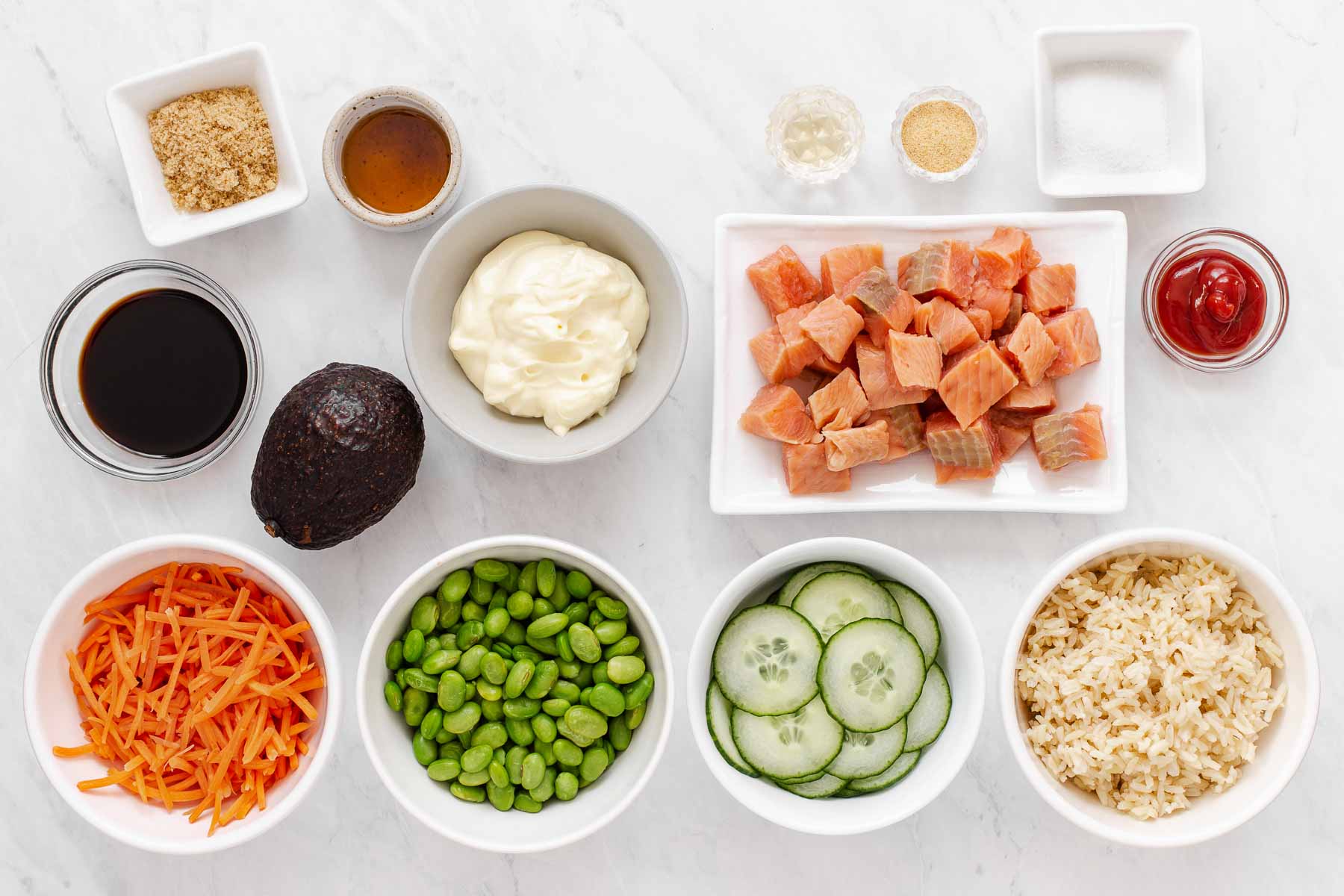 Bowls of fresh vegetables, cubed salmon, rice, and sauce ingredients on white counter.