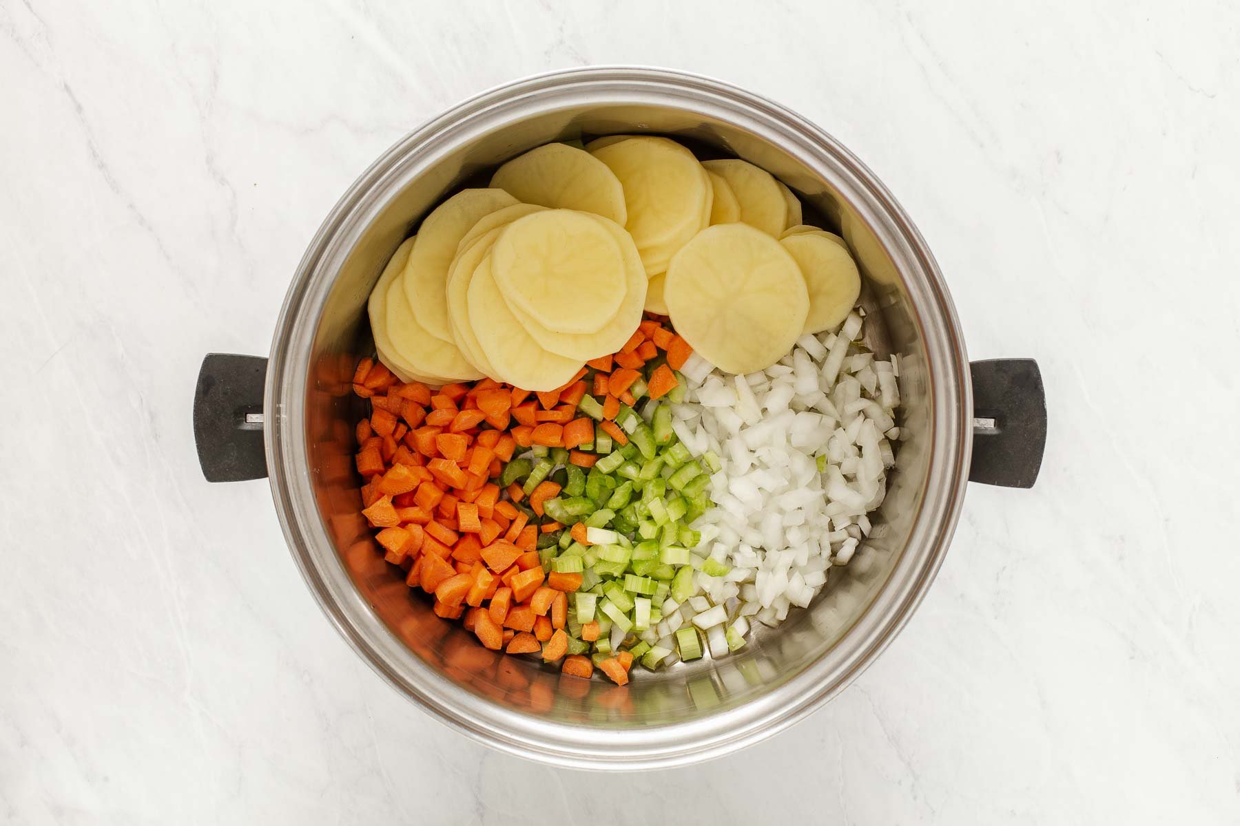 Silver soup pot with sliced potatoes, carrots, onion and celery.