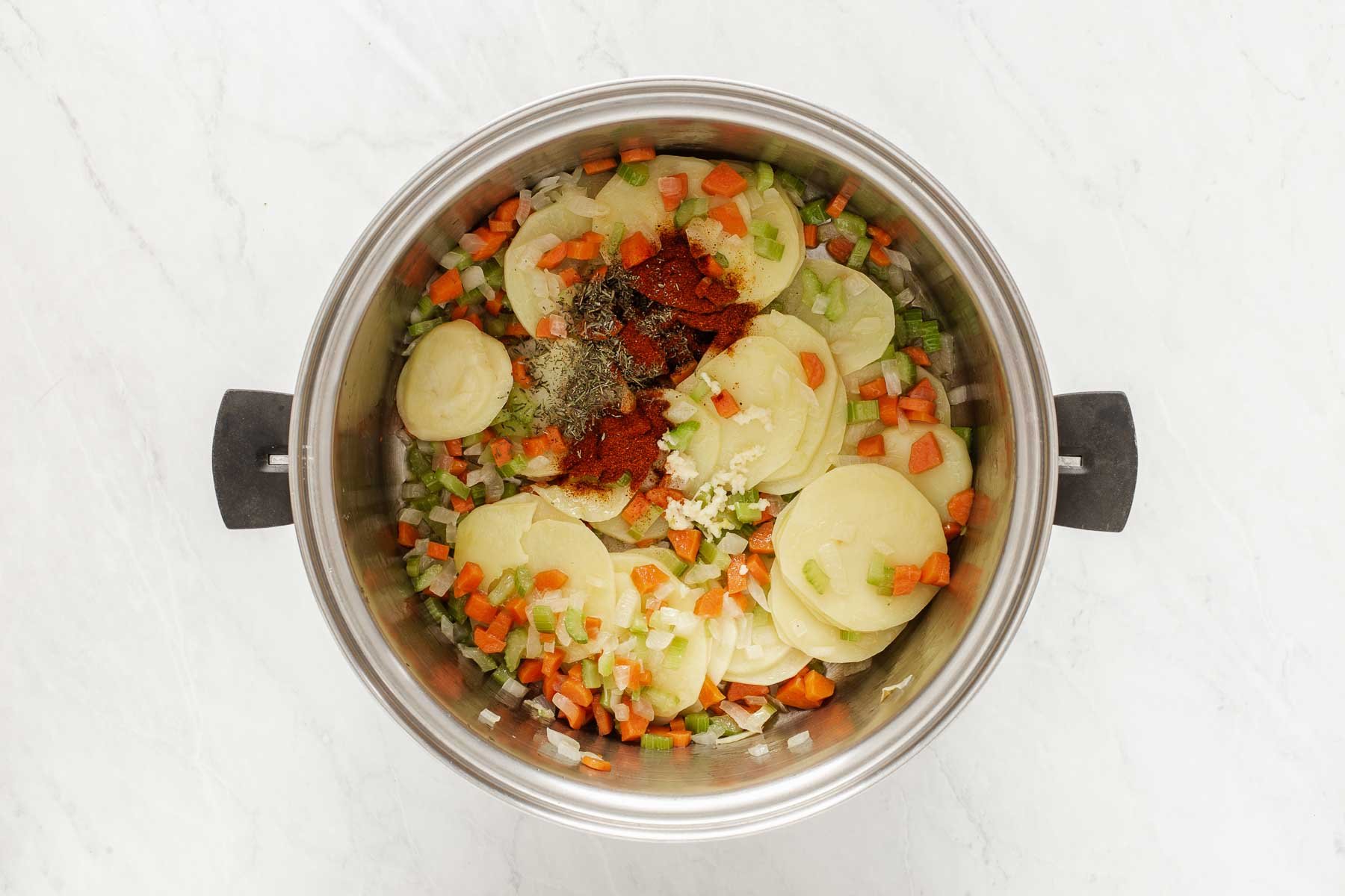 Stockpot with sliced potatoes, vegetables and spices.