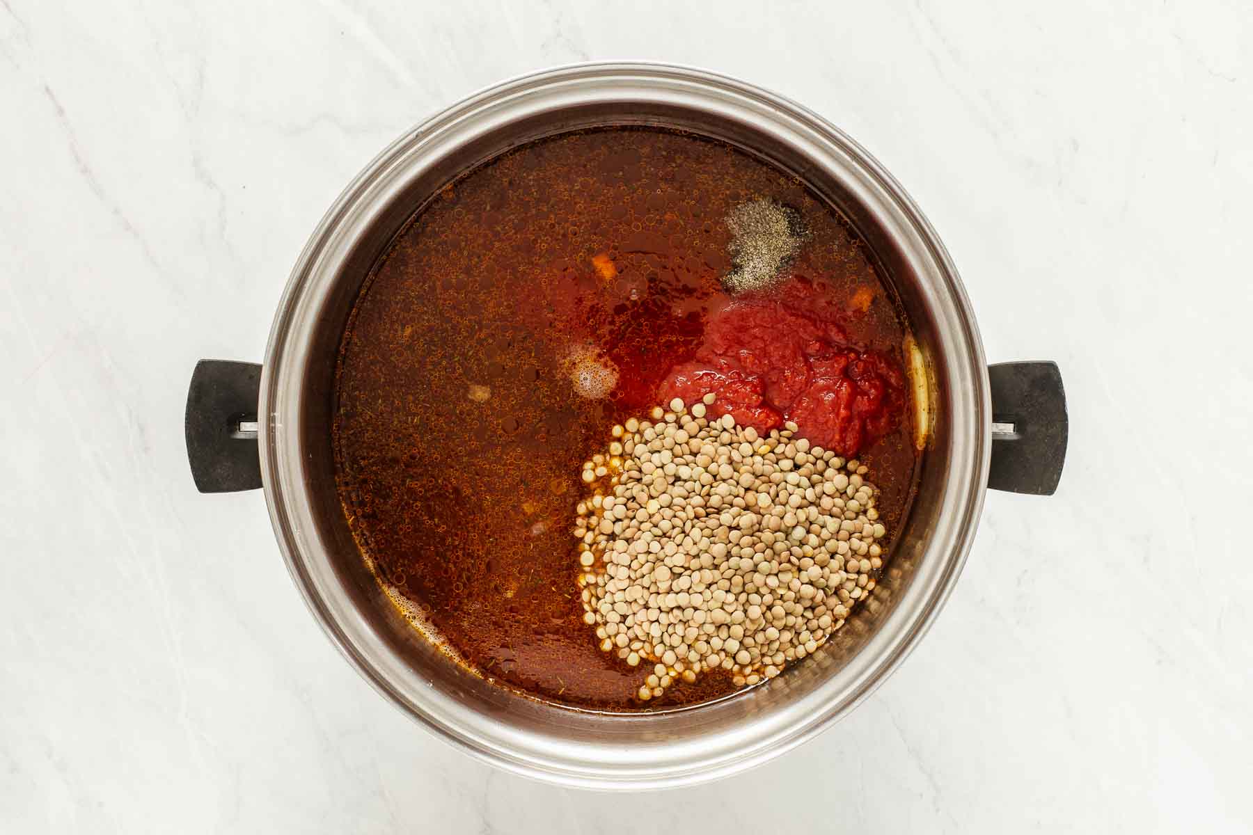 Pot of soup with crushed tomatoes, lentil and spices being stirred together.