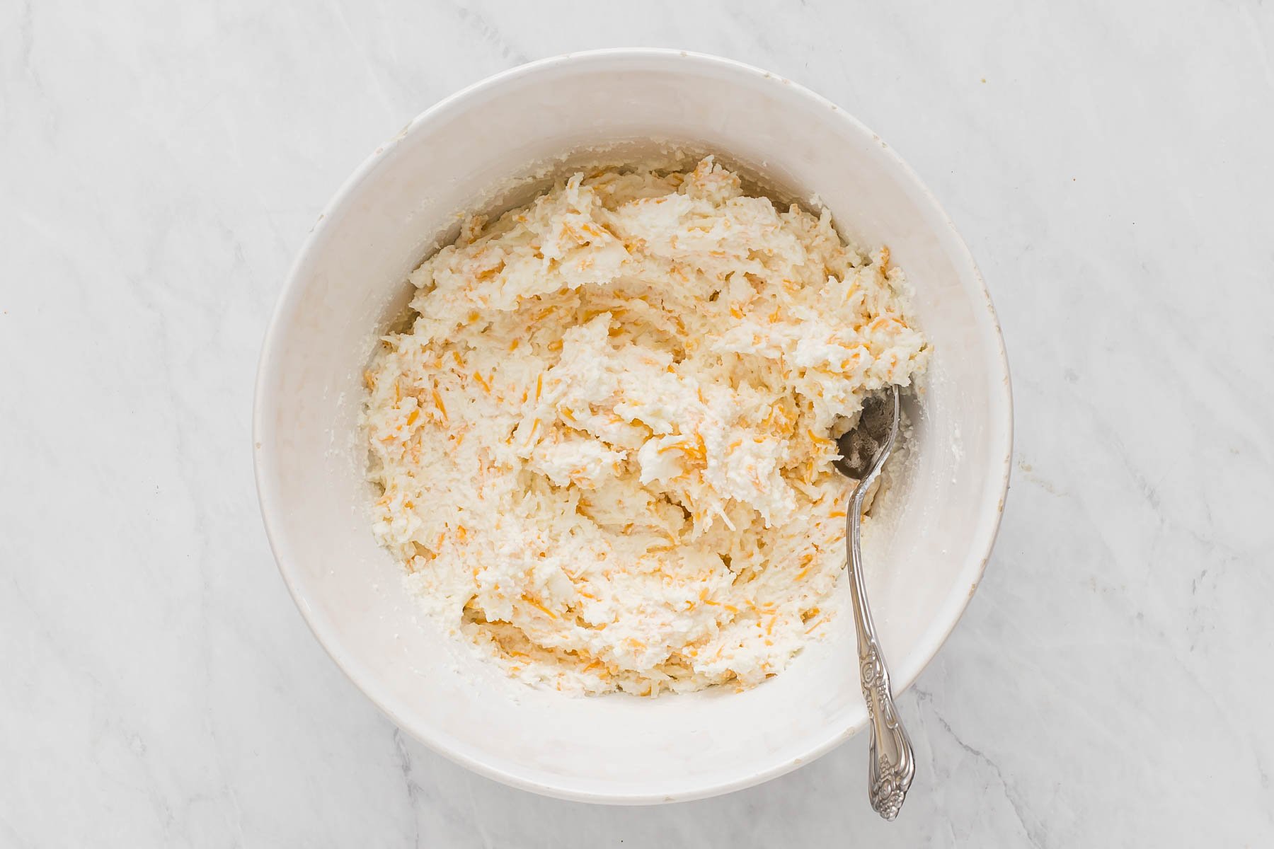 White bowl of ricotta cheese with yellow grated cheese mixed in.