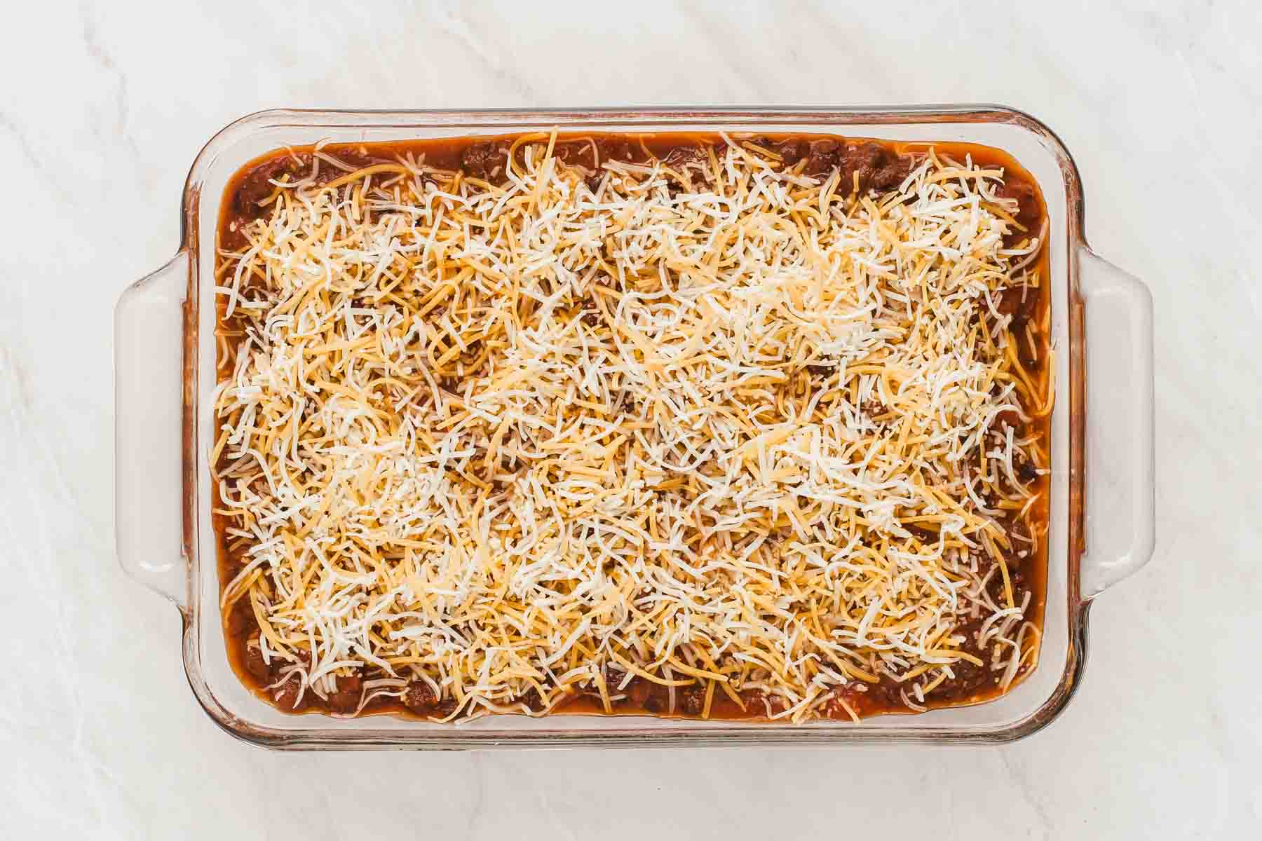 A pan of black bean lasagna with grated cheese on top, before being baked.