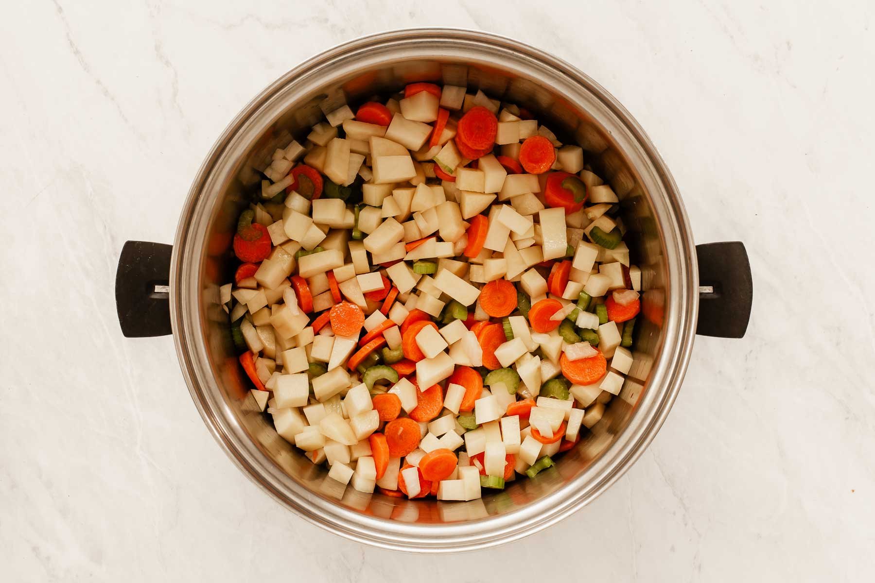 Large soup pot cooking cubed veggies in olive oil.