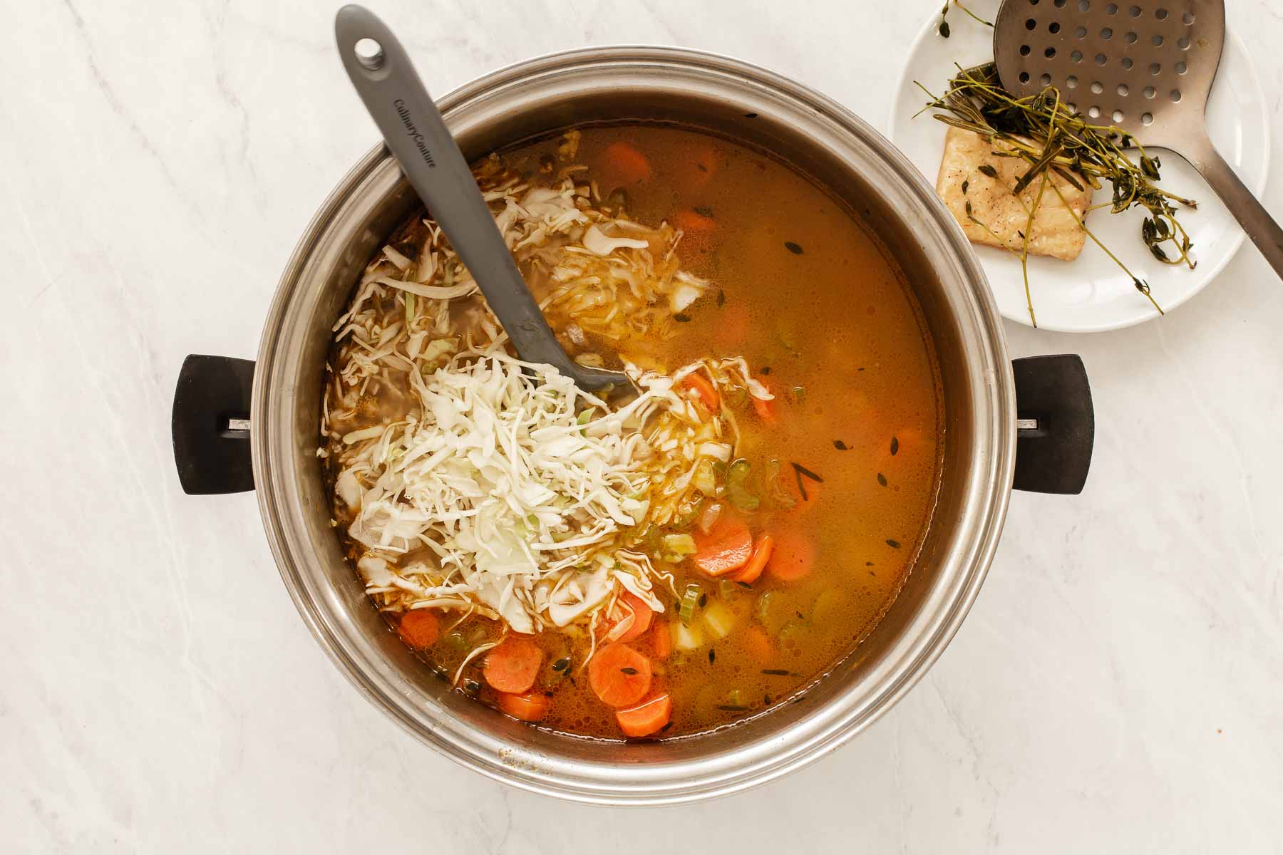 Stirring shredded Parmesan into yellow broth soup with carrots.
