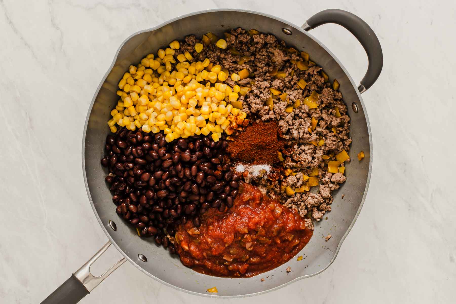 Grey skillet with ground beef, black beans, corn, salsa and chili spices.