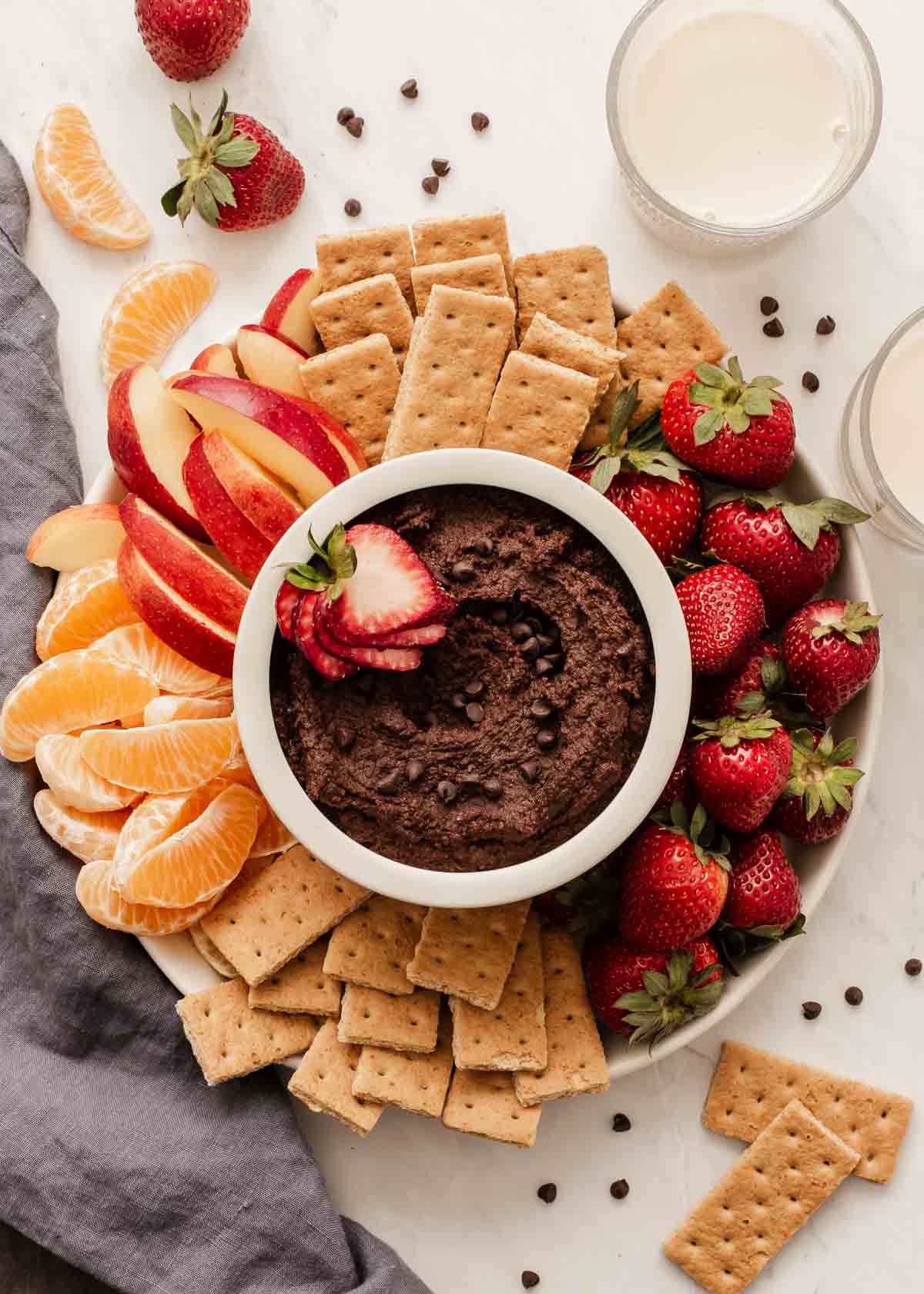 Overhead shot of brown appetizer in bowl surrounded by fresh fruit and graham crackers on plate.