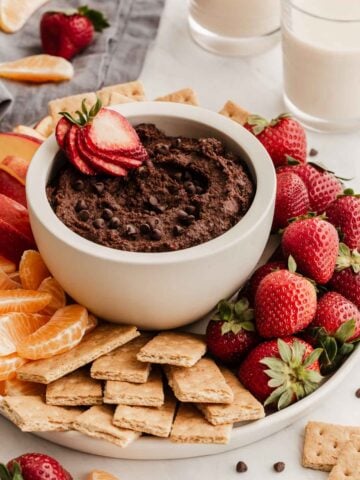 White bowl of chocolate hummus with strawberry inside.