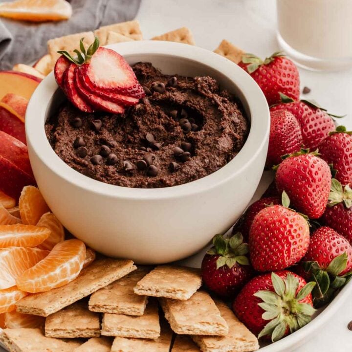 White bowl of chocolate hummus with strawberry inside.