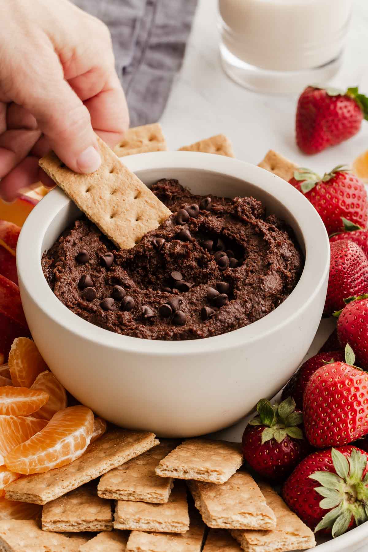 Hand dipping a graham cracker into a bowl of chocolate hummus with mini chocolate chips on top.