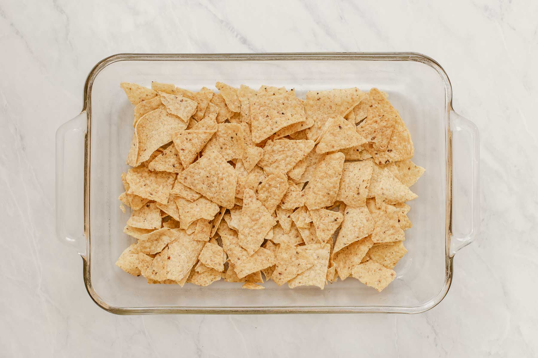 A 9x13 baking dish with crushed tortilla chips in the bottom.