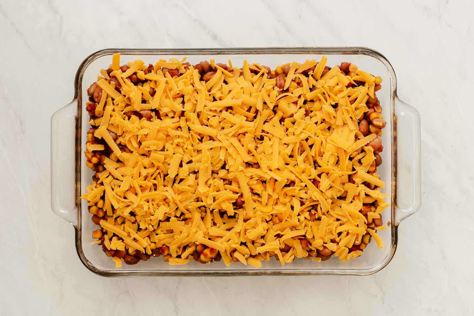 Pinto bean casserole in glass dish covered with shredded yellow cheese.