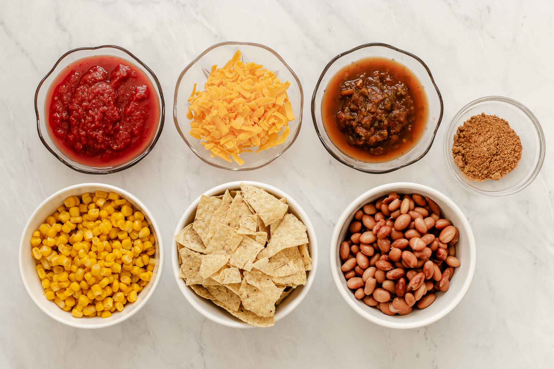 Bowls of beans, cheese, salsa and chips on white counter.