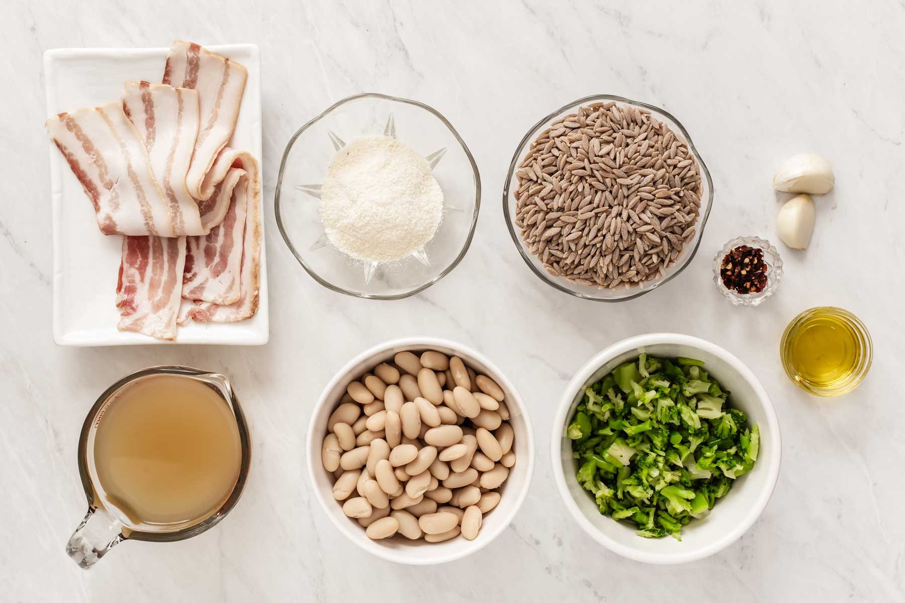 Bowls of orzo, beans, broth, bacon and broccoli on white counter.