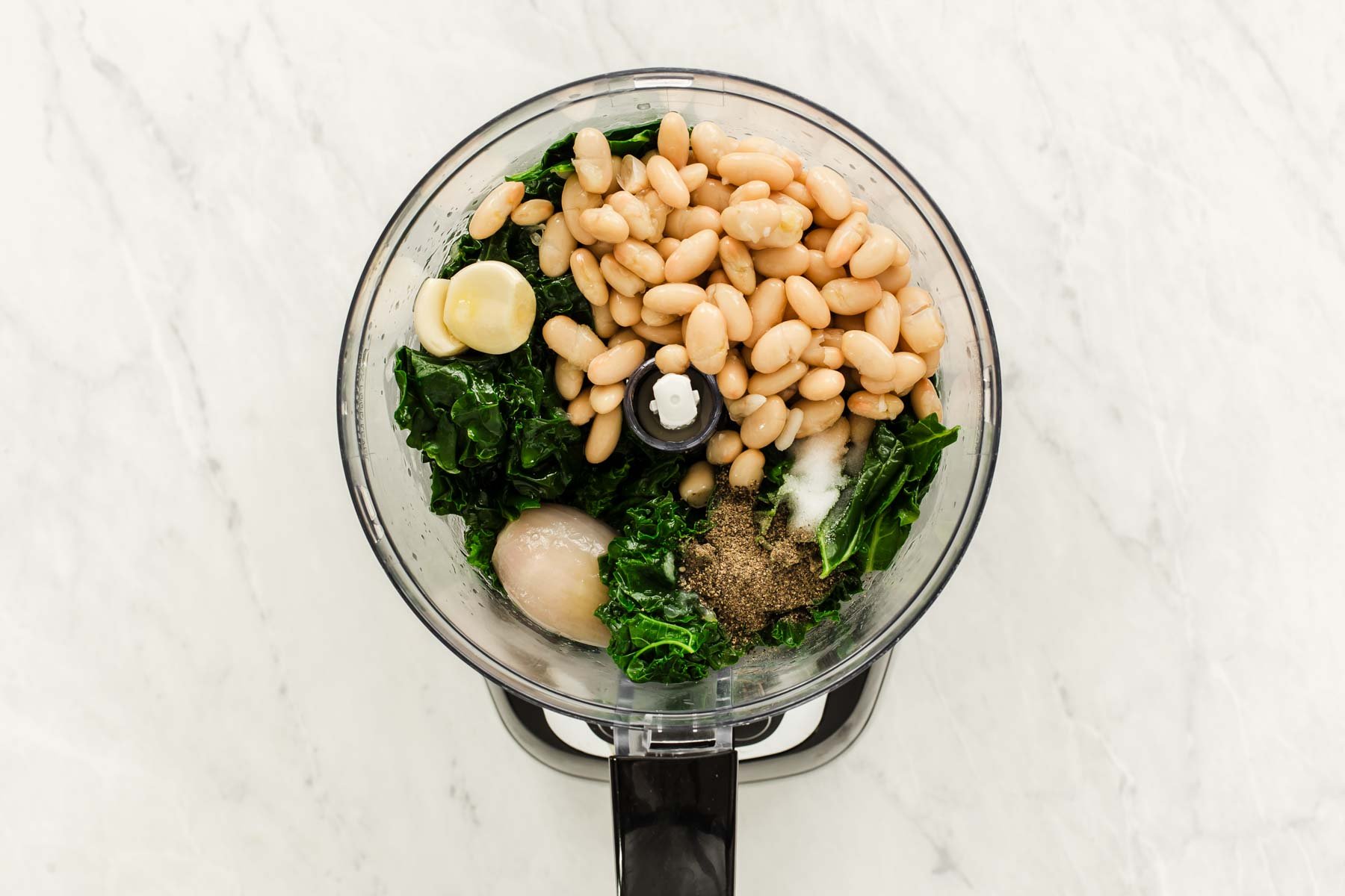 Mini food processor with white beans, greens, shallot and garlic cloves.