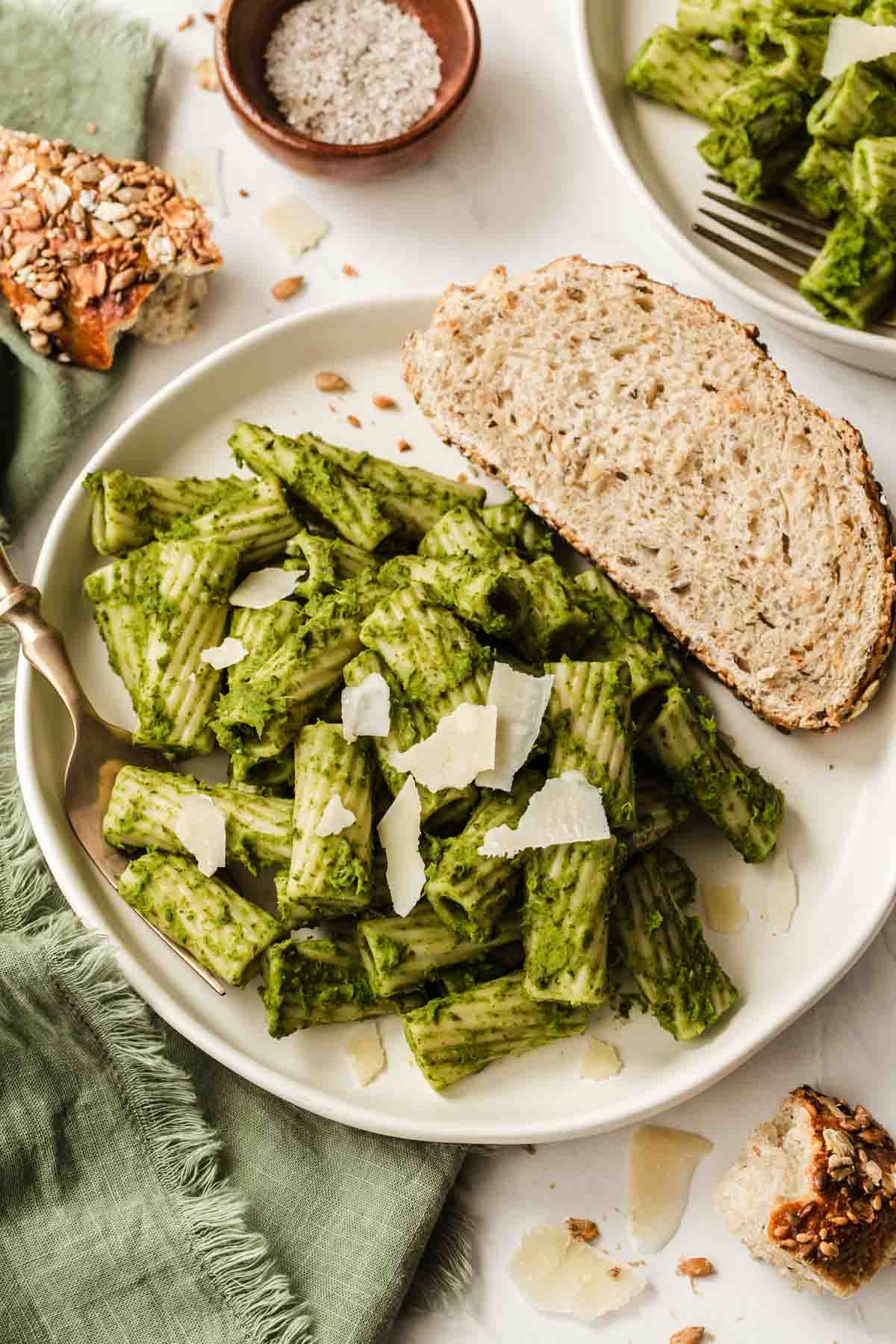 White plate of kale pesto pasta with sliced bread on side.