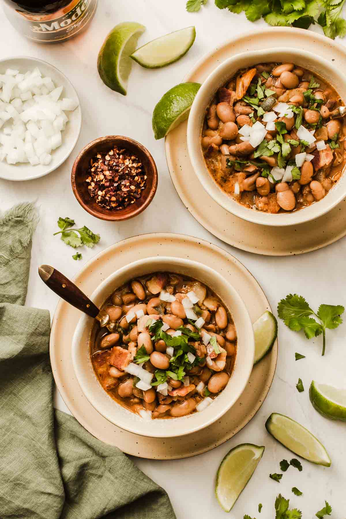 Two bowls of beans with spoons and garnishes.