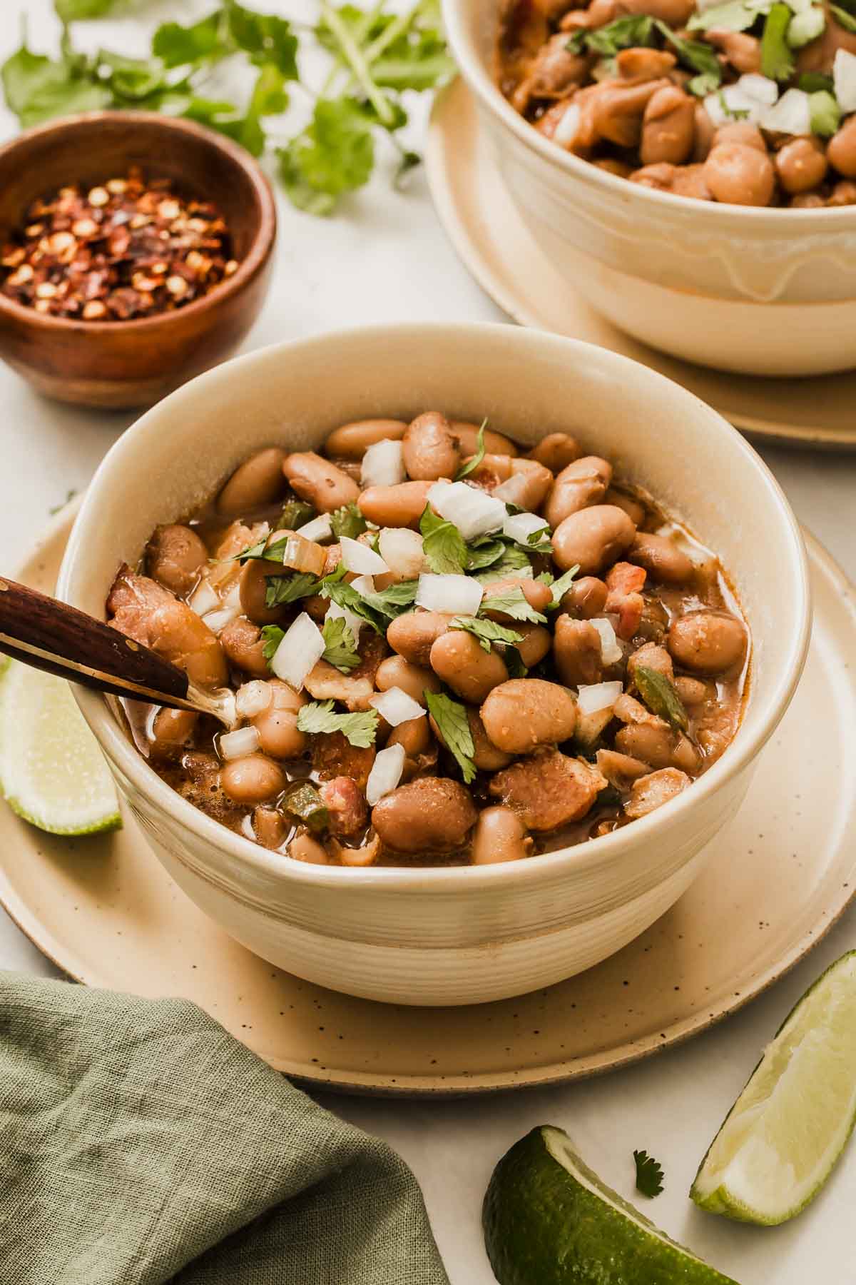 Cream bowl of brown pinto beans cooked into borracho beans garnished with onion and cilantro.