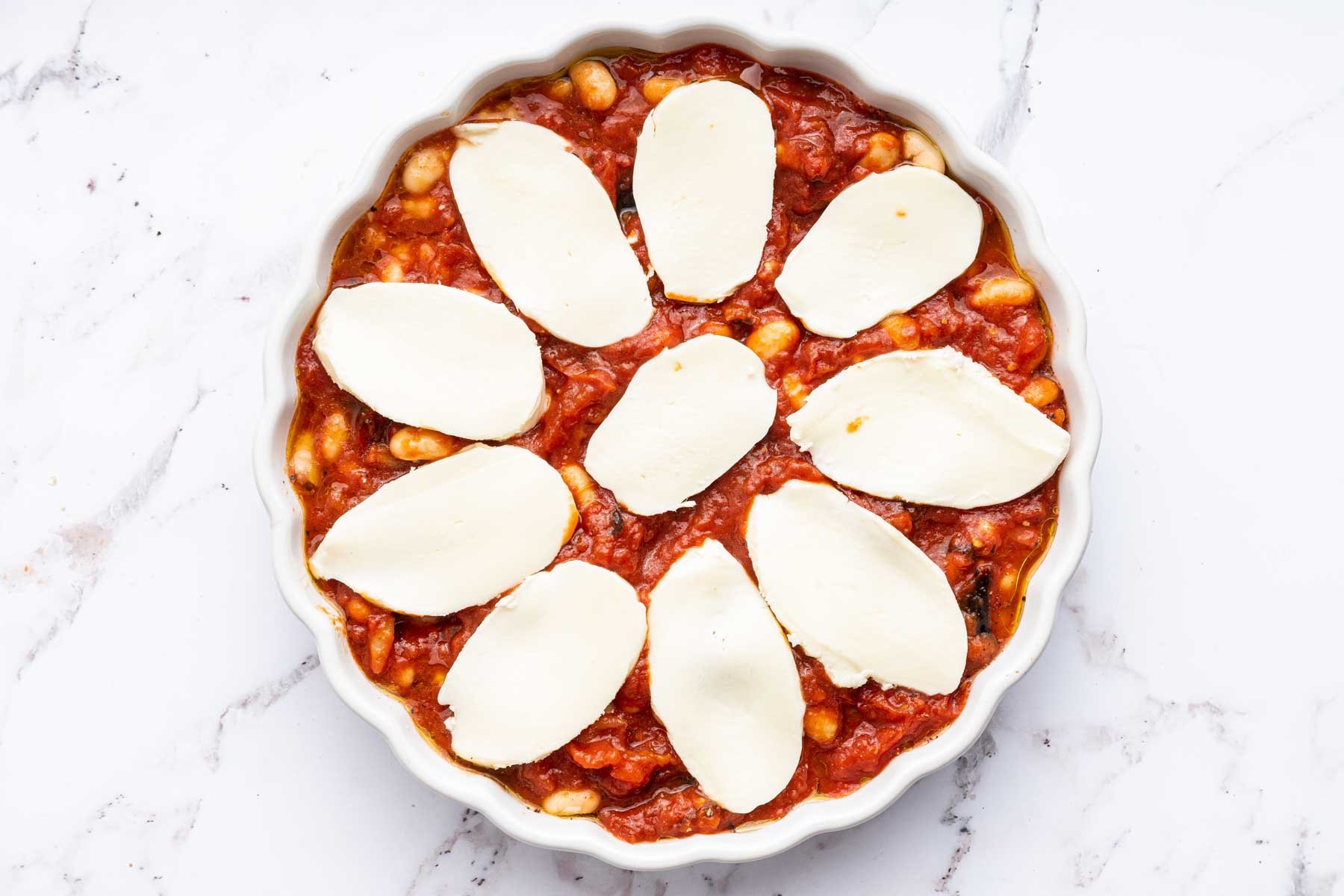 Round dish with red sauce and slices of oval mozzarella cheese on top.