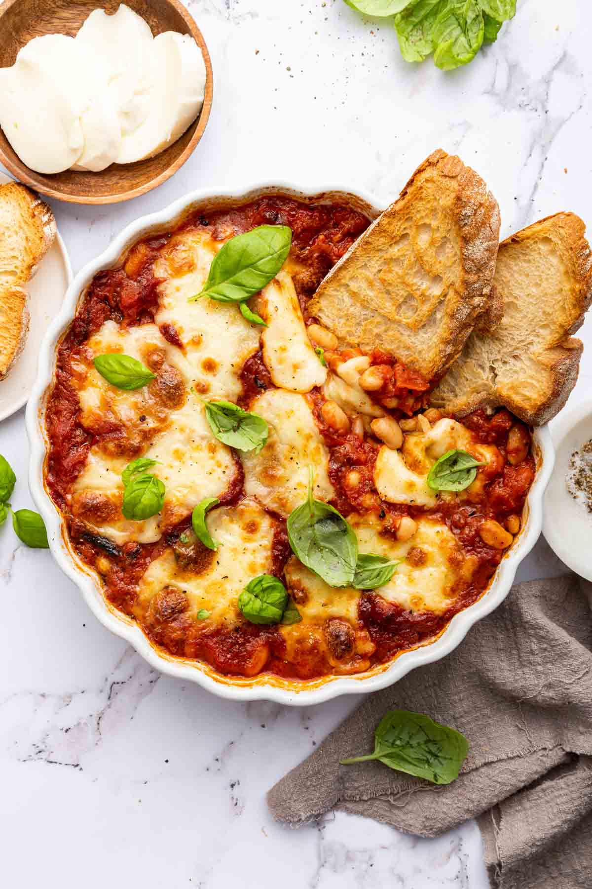 Vertical image of cheesy white bean tomato bake with sliced bread on side for serving.