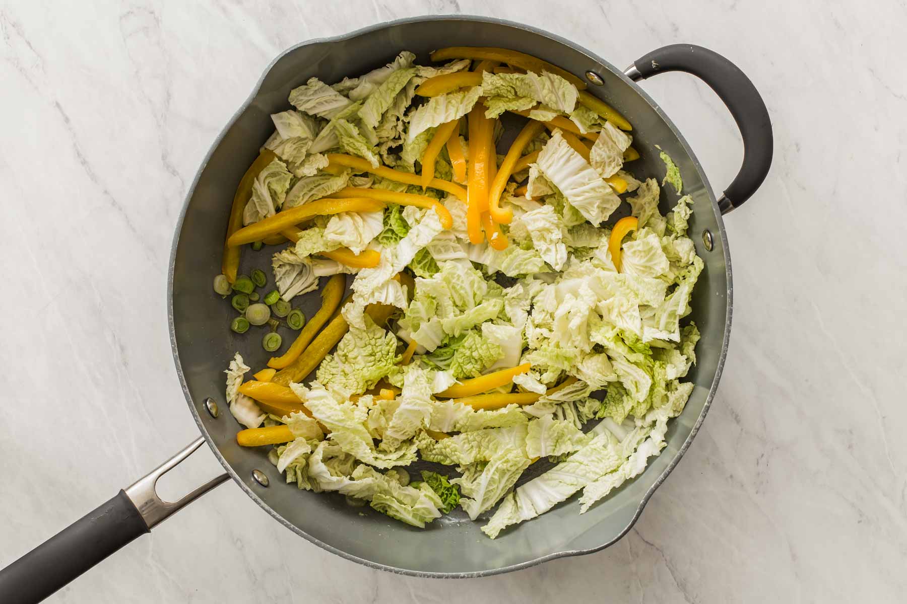 Grey skillet with cabbage, yellow bell pepper and green onions cooking.