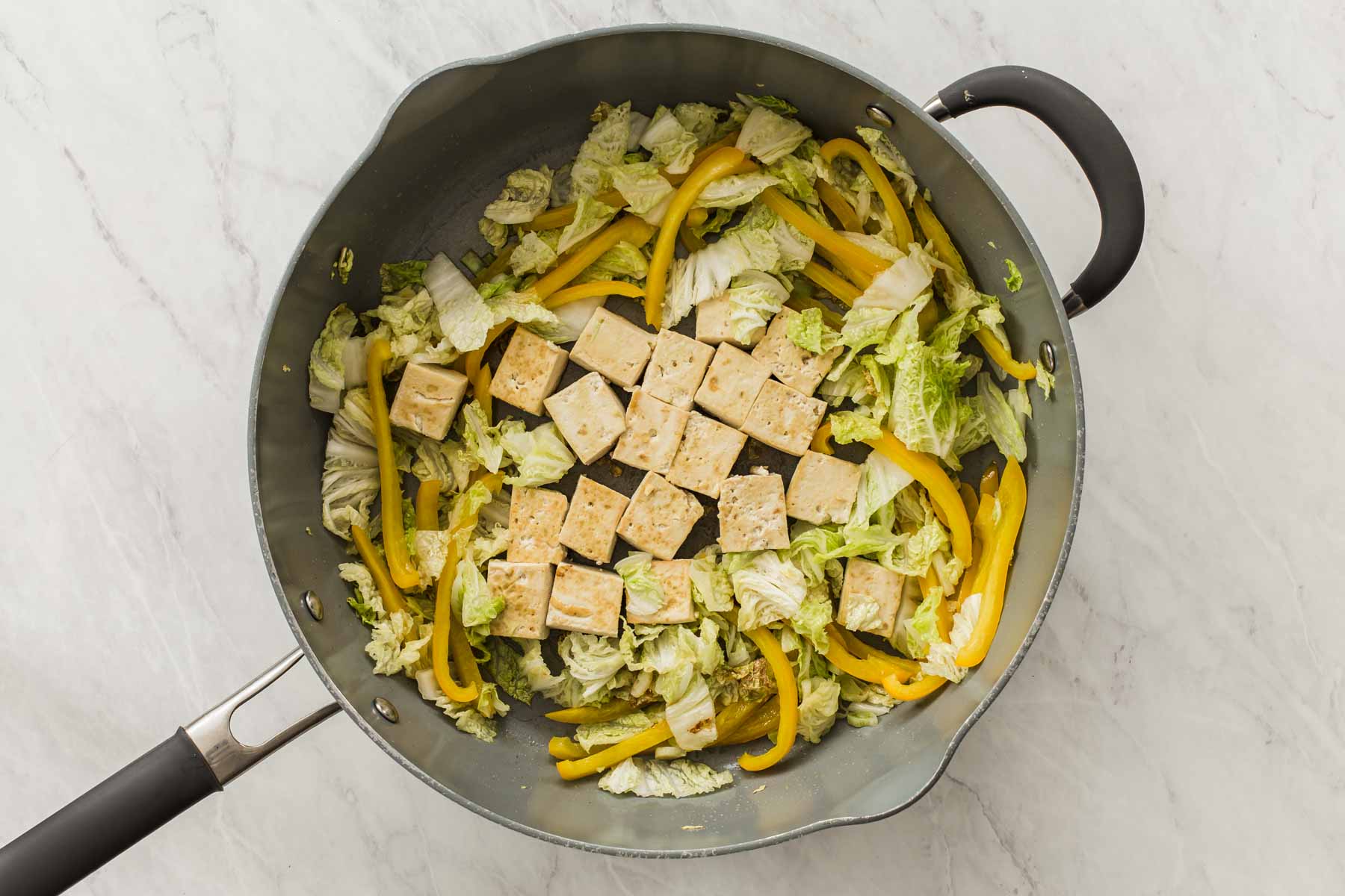 Adding tofu cubes to a skillet with stir fry vegetables.