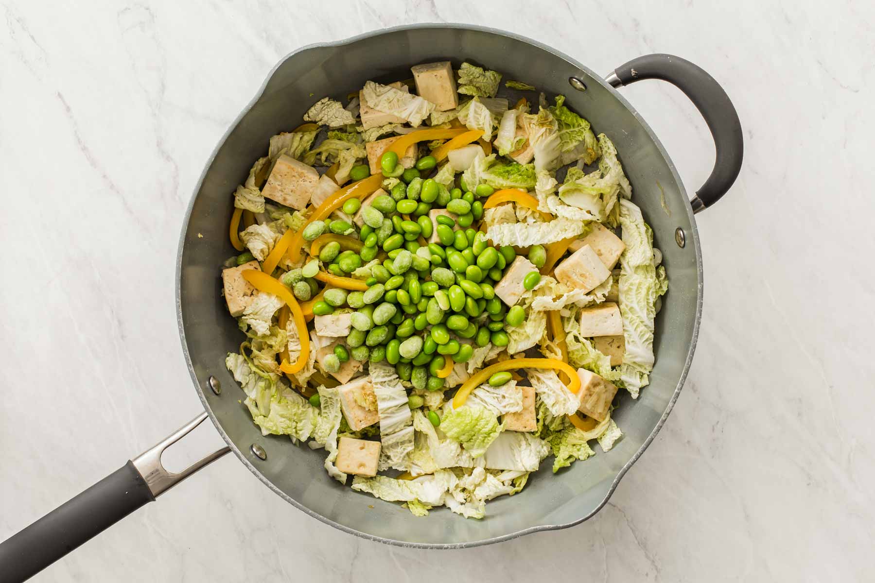 Adding frozen edamame to a skillet with stir fry vegetables.