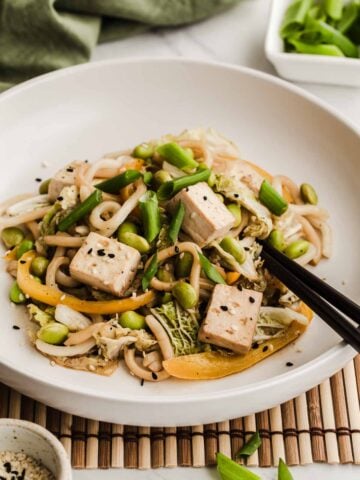 White bowl with edamame stir fry with noodles and tofu in it.