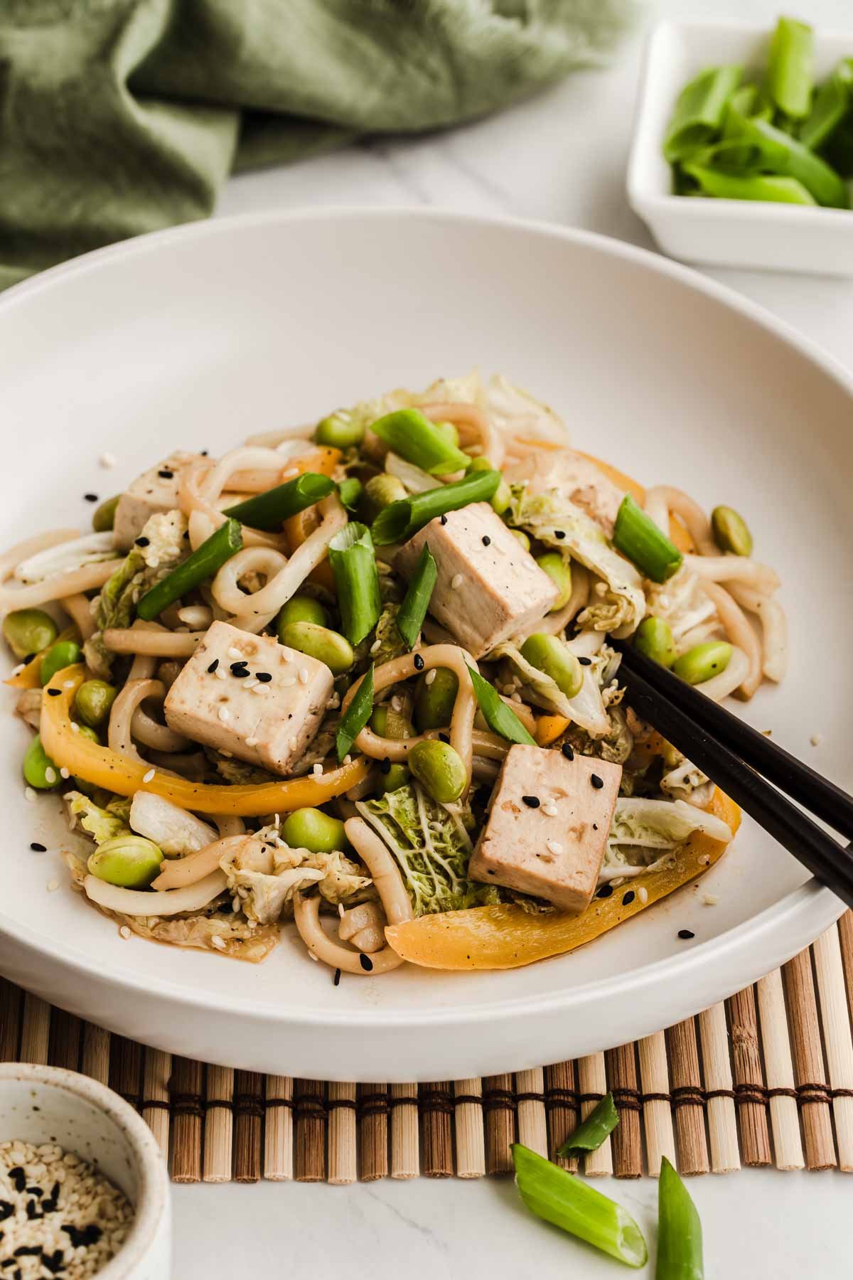 White bowl with edamame stir fry with noodles and tofu in it.