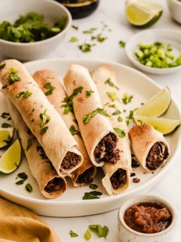 Black bean taquitos on a white plate sprinkled with cilantro.