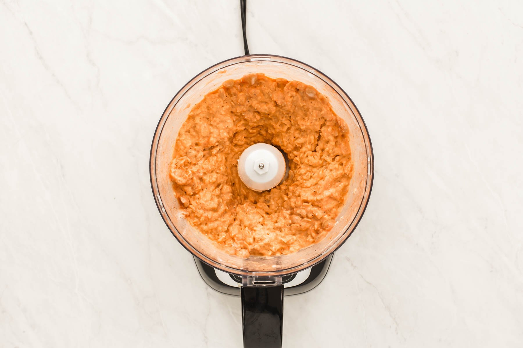 Open food processor bowl with creamy orange mixture inside.