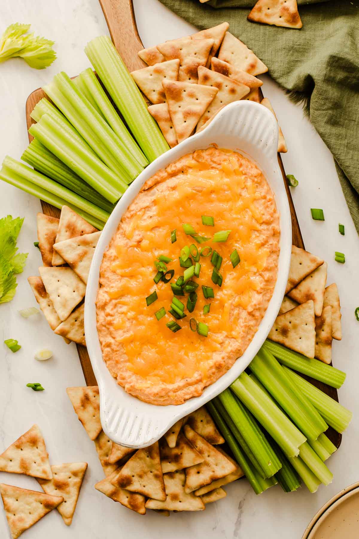 Overhead shot of buffalo chickpea dip in oval bowl with celery sticks and pitas on side.