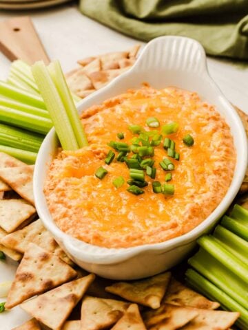 Three-quarter angle shot of orange buffalo chickpea dip in white oval dish with celery and pitas.