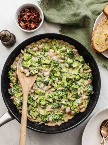 Overhead shot of broccoli and white beans in a skillet with a creamy sauce on top.